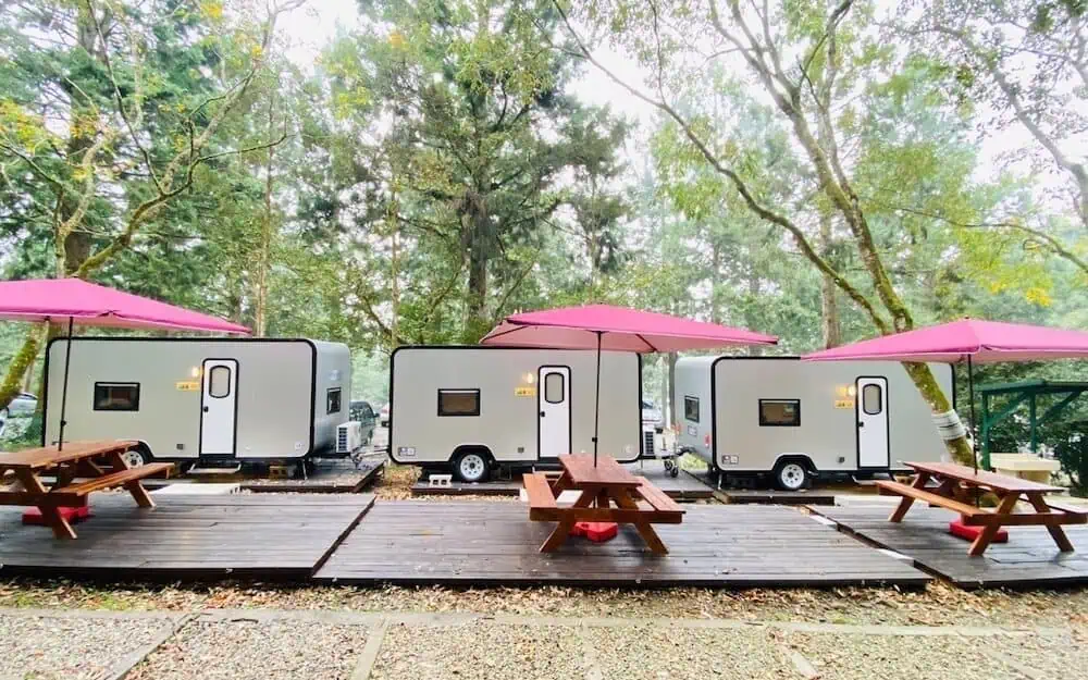 森林中的露營車，前方有戶外桌椅與紅色陽傘